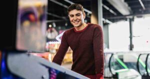 Portrait of a smiling handsome young man leaning on a pinball machine in an arcade game room